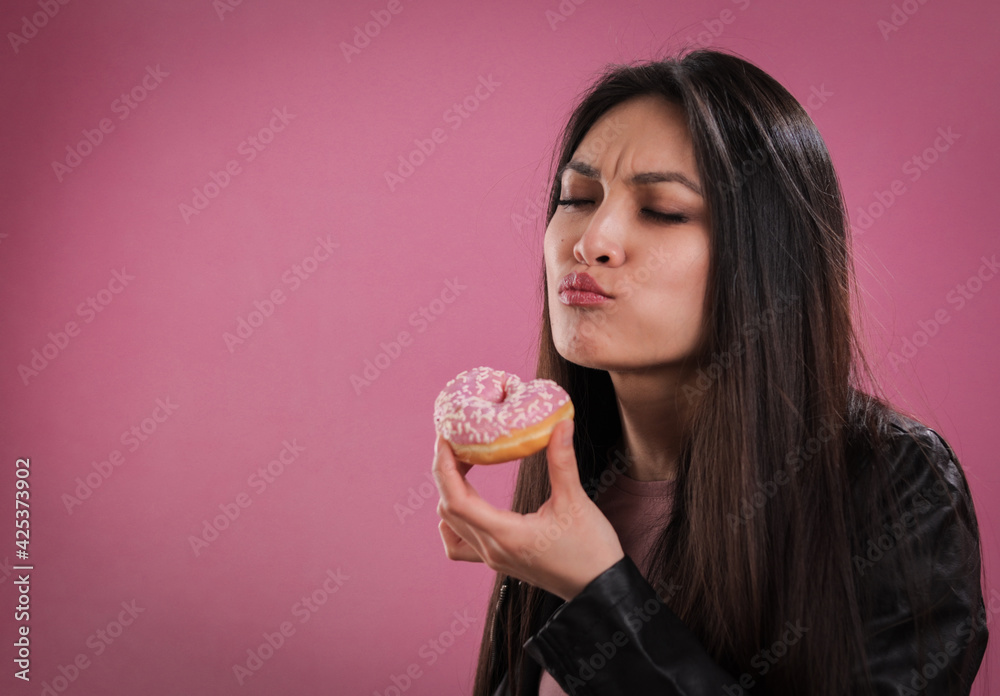 Young woman eats a doughnut against a pink background - studio photography Young woman eats a doughnut against a pink background - studio photography