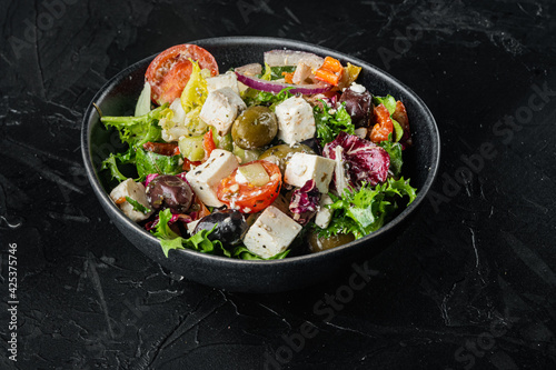 Traditional greek salad with fresh vegetables, feta and olives, on black background