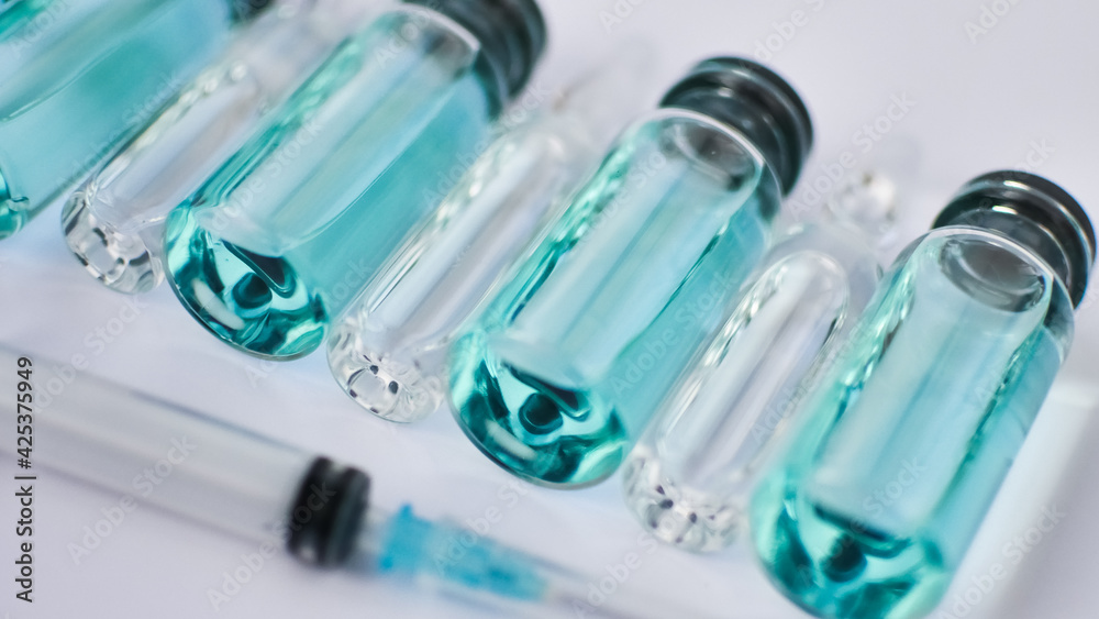 Vial vaccine, top view of glass ampoules with transparent and blue liquid, a syringe is lying near on white background, global vaccination concept Vial vaccine, top view of glass ampoules with transparent and blue liquid, a syringe is lying near on white background, global vaccination concept