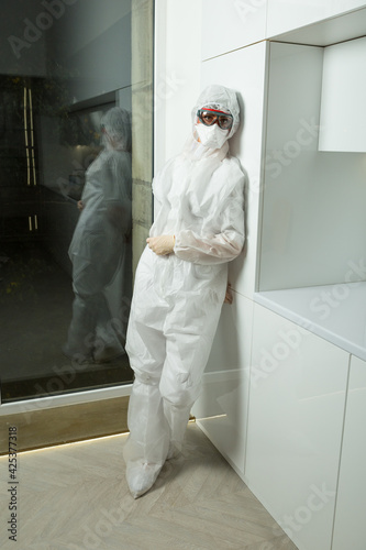 doctor wearing protective Suit, gloves, inhaler and protective glass stands near aumbry photo