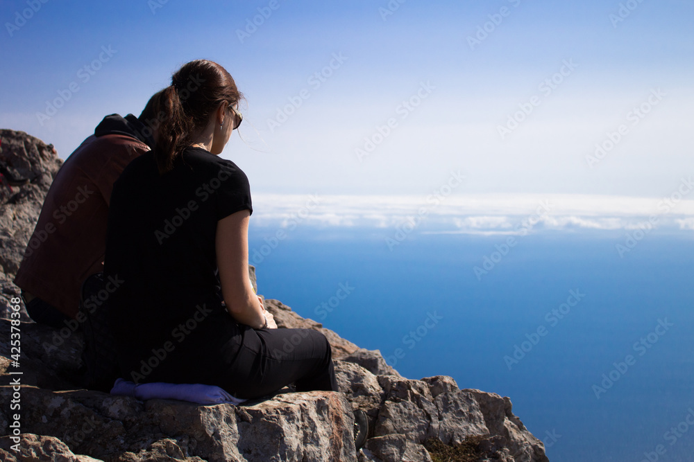 Two teenagers is sitting on top of the mountain.