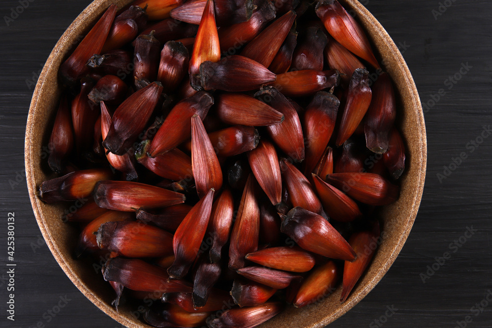 Typical araucaria seeds used as a condiment in Brazilian cuisine in winter. Brazilian pinion nuts in brown and red wooden bowl on gray wooden background Typical araucaria seeds used as a condiment in Brazilian cuisine in winter. Brazilian pinion nuts in brown and red wooden bowl on gray wooden background