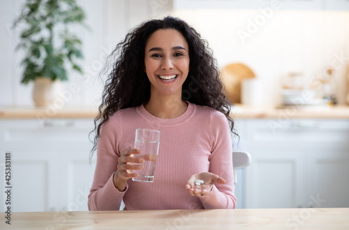 Happy Young Brunette Lady Holding Glass Of Water And Beauty Supplement Pills
