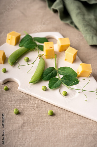 Fototapeta Naklejka Na Ścianę i Meble -  Ceramic cheese plate in the shape of a piece of cheese with pieces of cheese and herbs on it. green peas