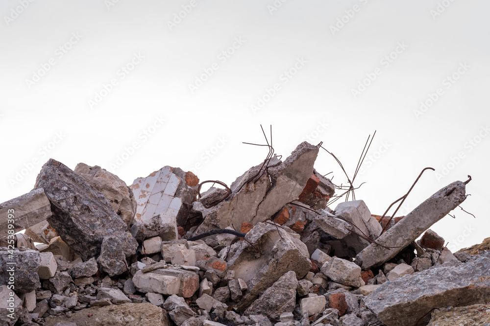Concrete fragments of a destroyed building with protruding rebar against the background of a uniform gray sky. Background.