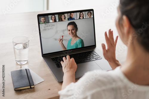 
remote online working woman on her laptop in home office on a desk while talking, flirting and waving hand in a video chat to greet team in a meeting watching video conference or webinar presentation