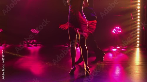 Elements Latin American dance performed by ballroom dancers. Rumba, cha cha cha, classical ballroom dance choreography in dark studio with colored rays of light. Silhouette. Legs close up. Slow motion