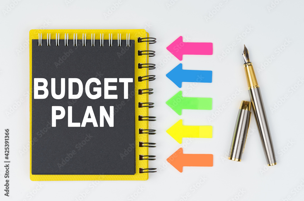 On a white background lies a pen, arrows and a notebook with the inscription - BUDGET PLAN On a white background lies a pen, arrows and a notebook with the inscription - BUDGET PLAN