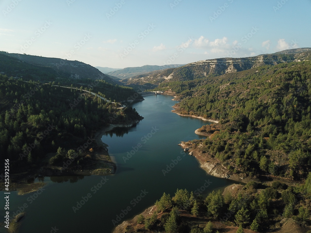 Aerial photography from a drone. Beautiful landscape with mountains and lake. Turquoise water and beautiful winding shores with coniferous forests against the blue sky. Cyprus