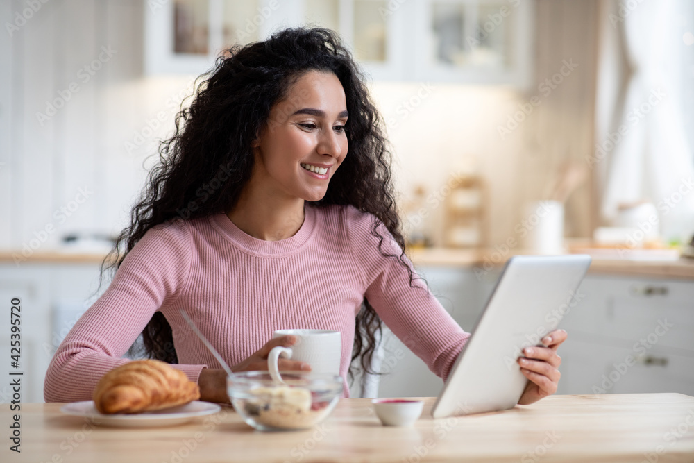 Smiling Young Woman Having Breakfast And Using Digital Tablet In Kitchen Smiling Young Woman Having Breakfast And Using Digital Tablet In Kitchen