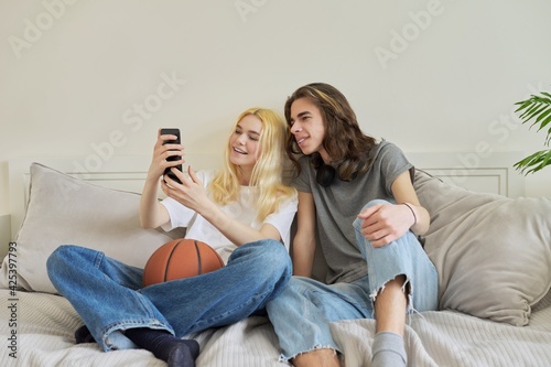 Happy laughing hipster teenagers male and female having fun using smartphone