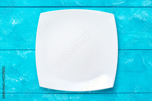 Empty white plate on blue wooden table. Top view. Mockup for food project.