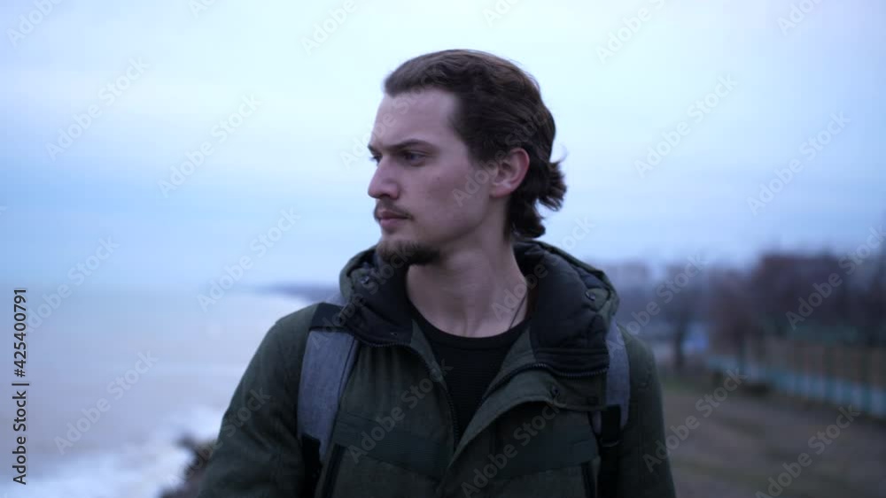 Portrait of a lonely depressive man with curly hair and beard walking on a cliff above sea in cloudy autumn day Portrait of a lonely depressive man with curly hair and beard walking on a cliff above sea in cloudy autumn day