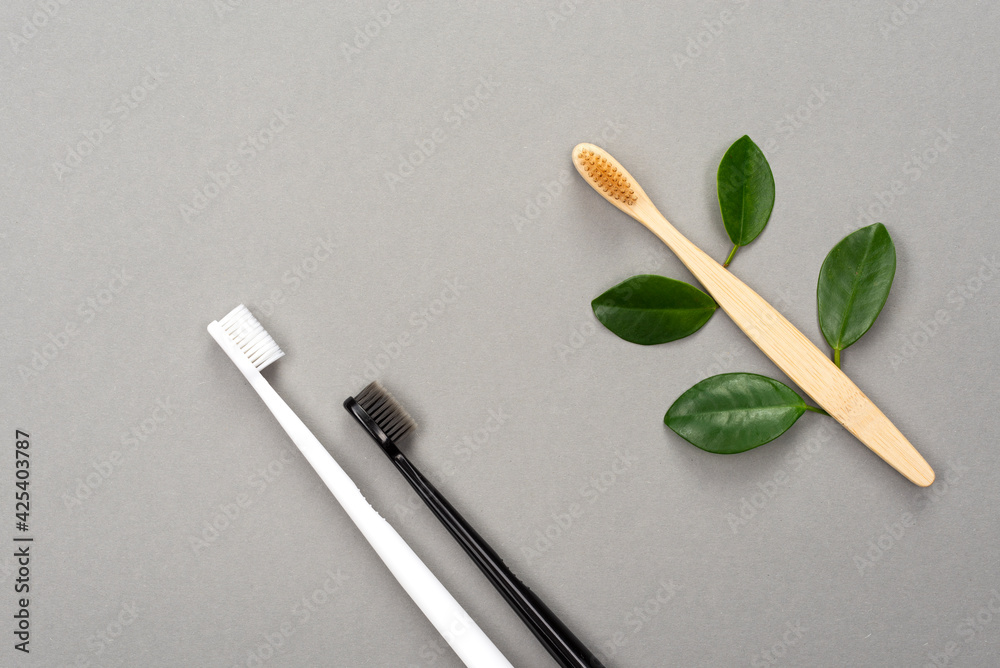 Natural eco friendly bamboo toothbrush and plastic toothbrush on gray background. Choose a plastic or wooden toothbrush. Recycling concept, no waste, no plastic, top view