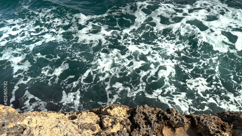 Top view of the foamy waves of the sea near the cliffs. Dark blue sea