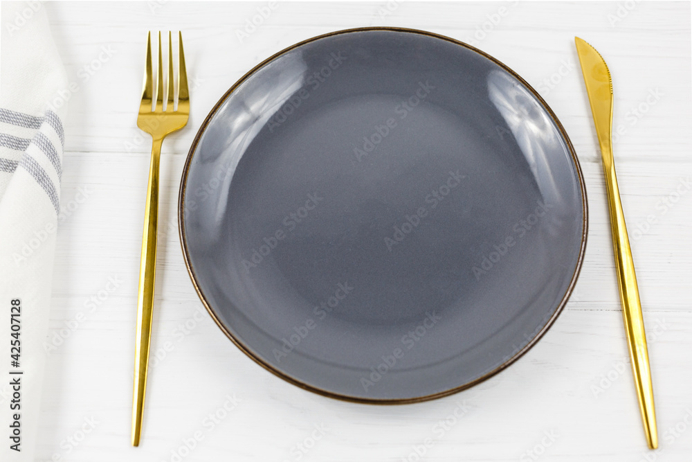 Gray empty plate with fork, knife white striped textile napkin on wooden table. Golden cutlery, table setting utensils. Mock up Gray empty plate with fork, knife white striped textile napkin on wooden table. Golden cutlery, table setting utensils. Mock up