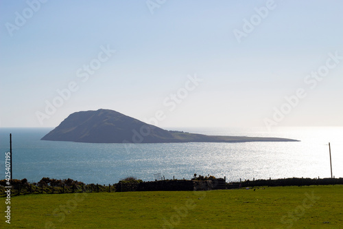 Wales, dramatic beautiful Bardsey island. Medieval pilgrimage destination. Isolated remote landscape with foreground of green fields and the calm sea with sun glinting, in the distance. Copy space. photo