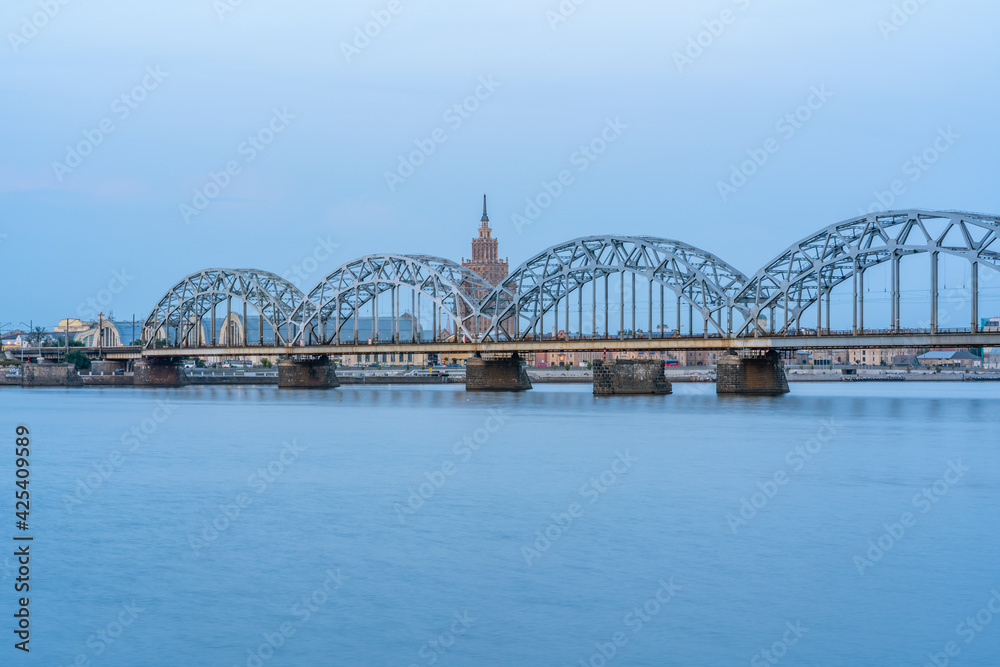 Fototapeta premium Cityscape with Railway Bridge in Riga, Latvia, on Blue Hour over River Daugava