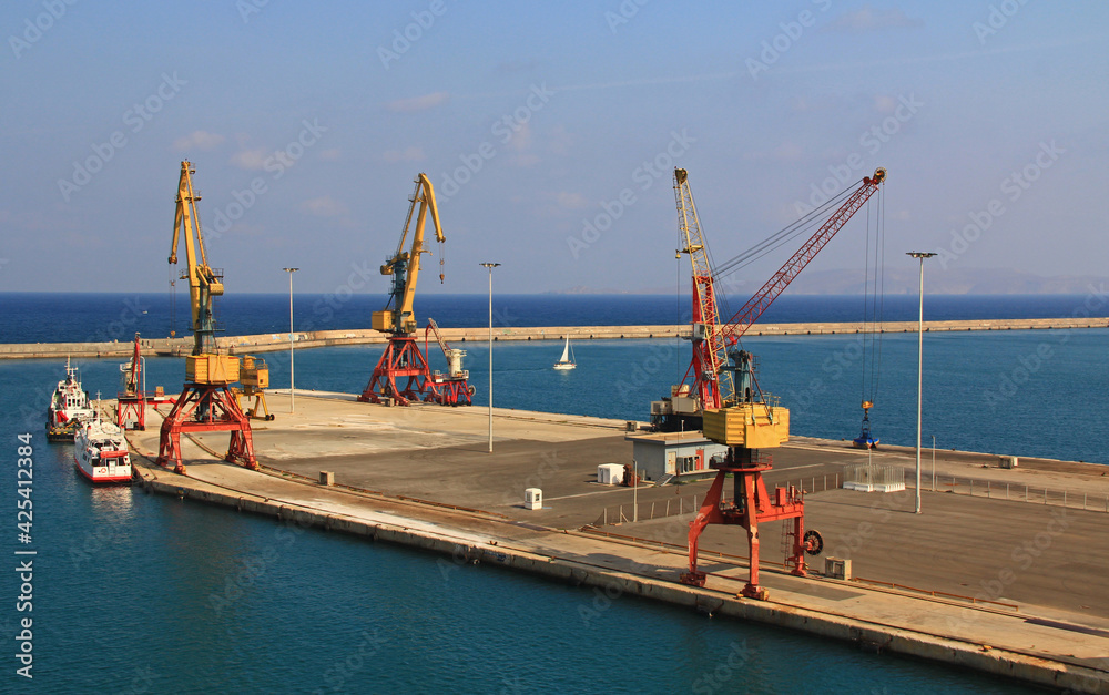 Harbor with industrial loading dock for ships in Heraklion, Crete, Greece with a cruise ship docked nearby, tug boats and blue sky copy space.