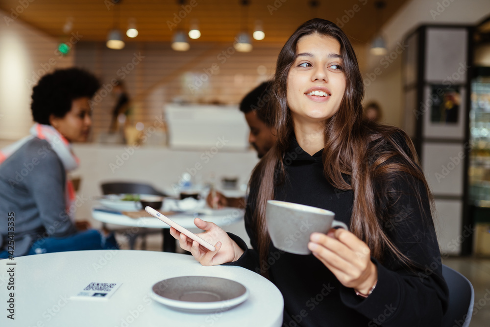 Female student using smartphone while sitting in cafe