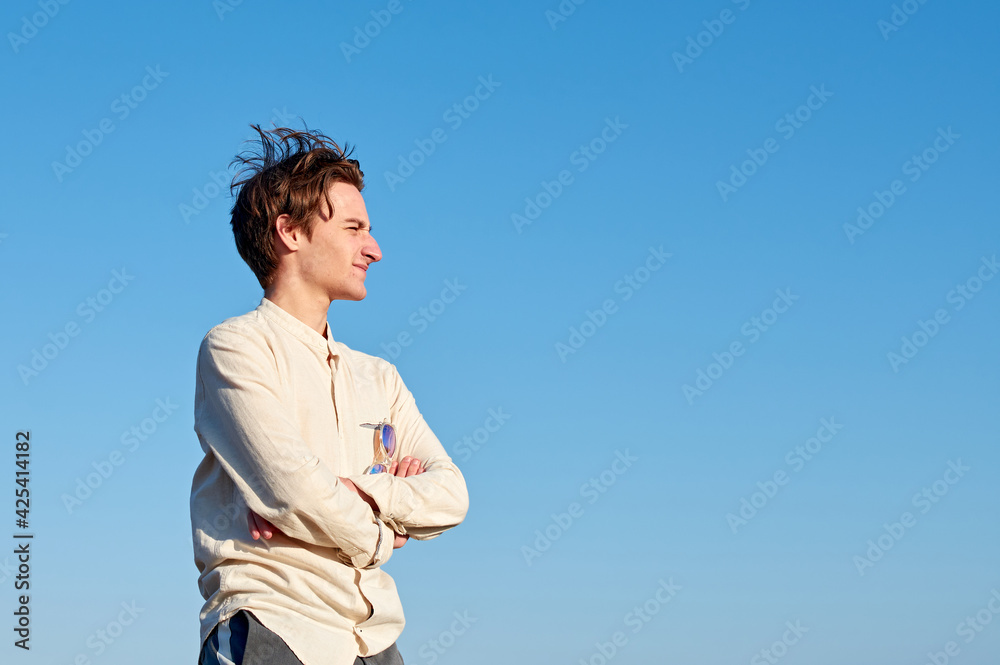 A Caucasian man from Spain in a beige shirt with glasses hanging off of him on clear sky background