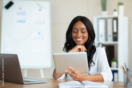 Joyful black business lady using tablet pc at workplace, speaking to colleagues on webcam, copy space