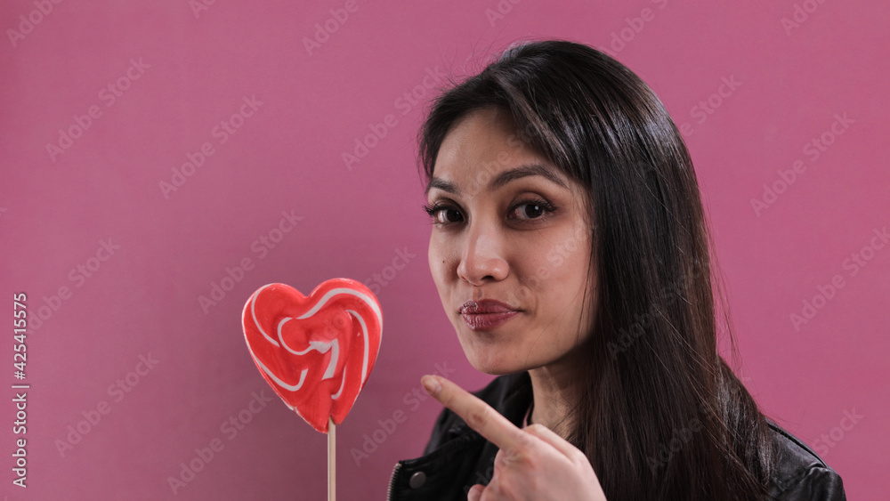 Young pretty woman holds a big heart-shaped lollipop - studio photography Young pretty woman holds a big heart-shaped lollipop - studio photography