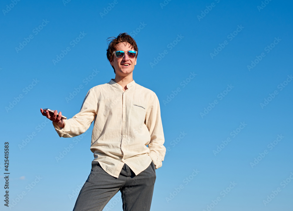 A Caucasian man holding his phone and smiling while looking forward with one hand in pocket