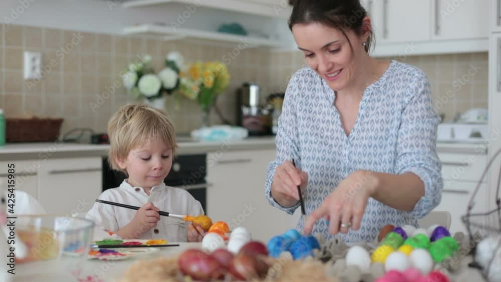 Beautiful blond child, toddler boy, painting easter eggs with mother at home, making easter wreath with rainbow colors Beautiful blond child, toddler boy, painting easter eggs with mother at home, making easter wreath with rainbow colors