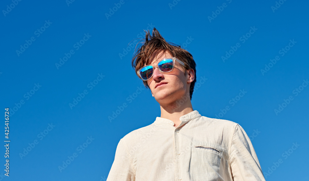 A Spanish white man with long hair, purple glasses and a beige shirt staring into the distance on clear blue sky background A Spanish white man with long hair, purple glasses and a beige shirt staring into the distance on clear blue sky background