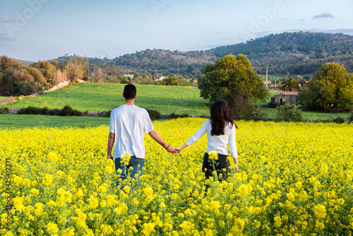 Couple walking through the freshly flowered field. Young couple in a field in spring holding hands. Spring arrives.