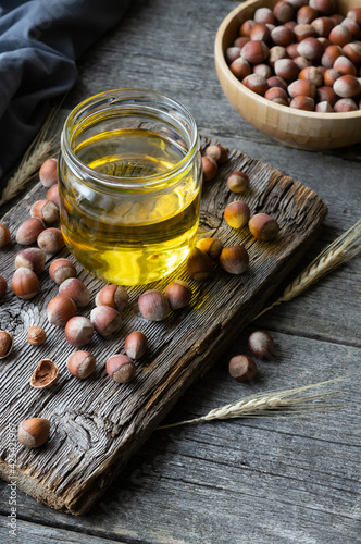 Hazelnut oil, filbert and cooking oil in glass of jar on wooden backdrop, heap or stack of hazelnuts, healty food