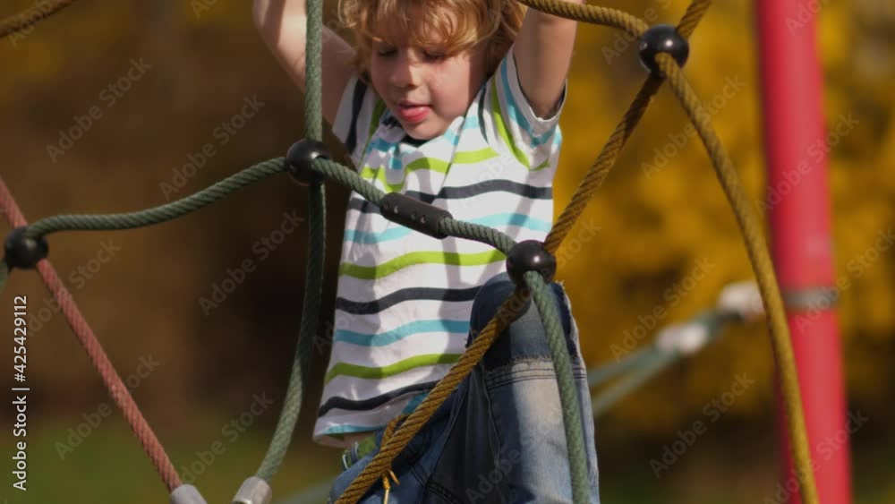 Blonde boy plays in the playground and climbs over monkey bars Blonde boy plays in the playground and climbs over monkey bars