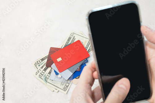 Heap of credit cards and many banknotes of 20 dollar on white background with blurred person paying online via mobile phone, depth of field. Cconsumer lifestyle, transaction internet banking concept. photo