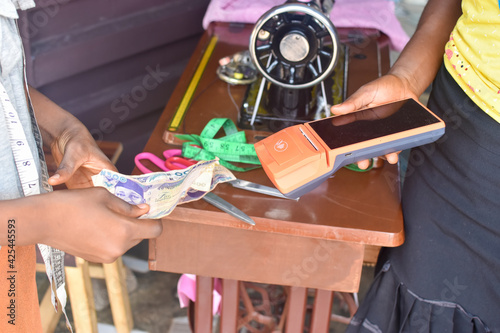 Tendering Nigerian naira note in a cash transaction with the help of POS machine in a tailoring shop 