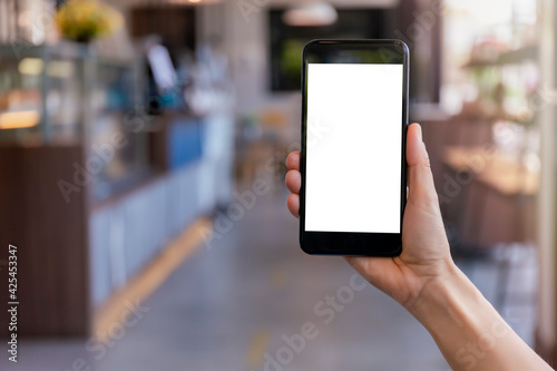 Hand women holding black mobile phone with blank white screen with blur coffee shop background. Mockup image of hand holding smartphone with blank white screen with copy space