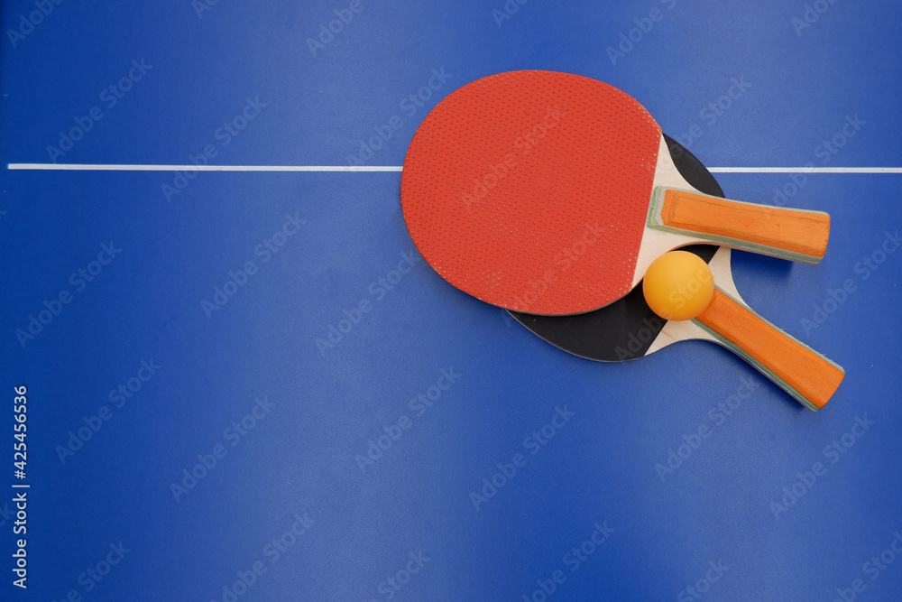on the tennis table is a ball and two table tennis rackets. on the tennis table is a ball and two table tennis rackets.