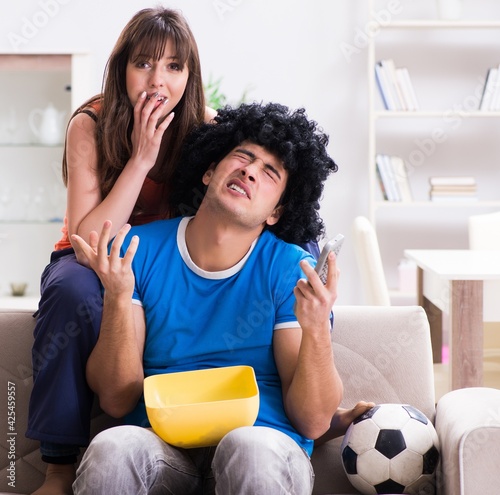 Young man watching football with his wife at home