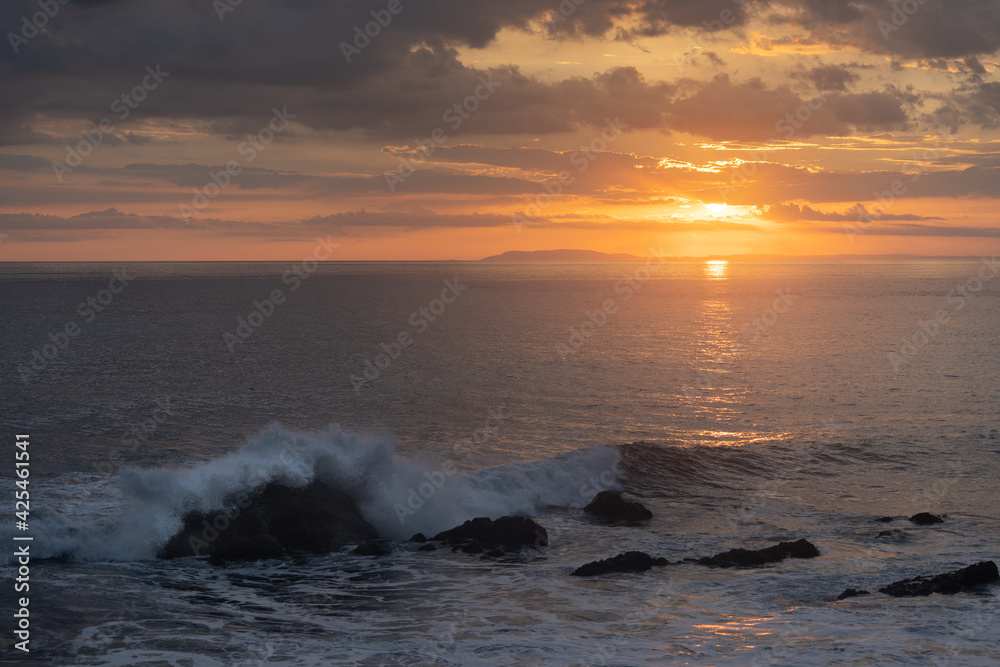 Beautiful view of the ocean waves chasing in rocks with a magical sunset in the horizon