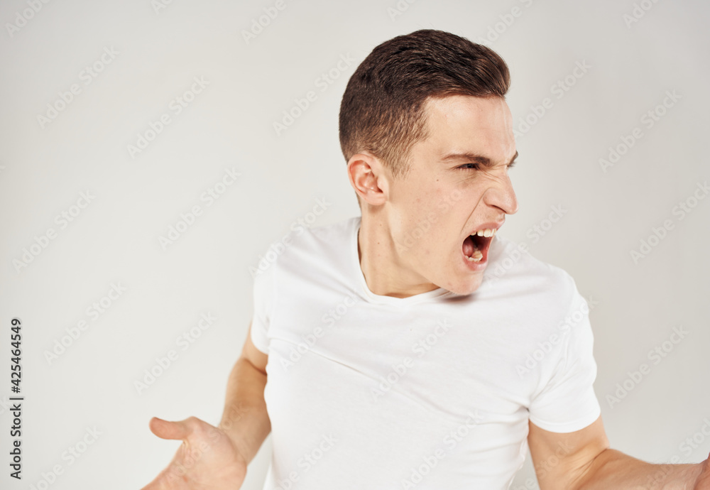 Obraz premium A man in a white T-shirt gestures with his hands on a gray background stress irritability 