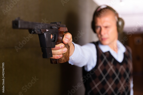 Focused shooter practicing sport handgun shooting at firing range. Selective focus on male hand squeezing pistol grip and pressing trigger.