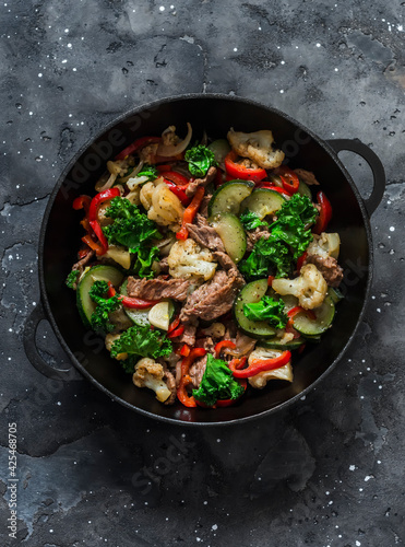 Quick beef stew with zucchini, cauliflower, sweet pepper, kale in a cast-iron pan on a dark background, top view