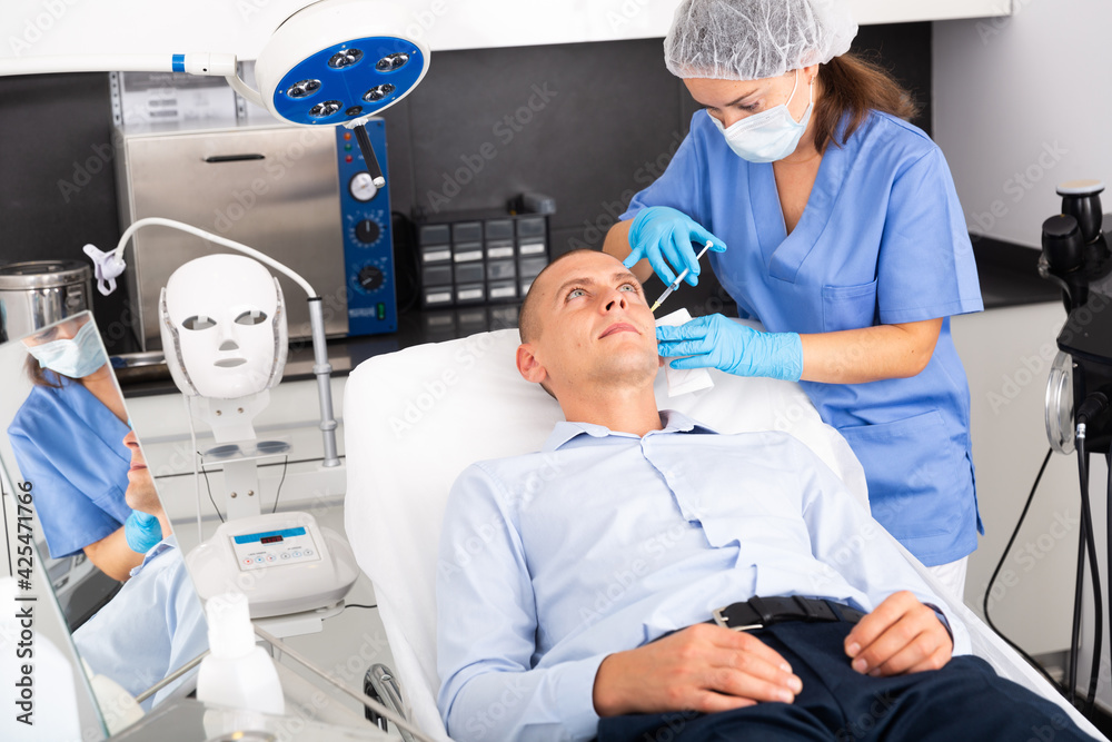 Obraz premium Skilled woman beautician filling males wrinkles using rejuvenating injections in clinic of aesthetic medicine