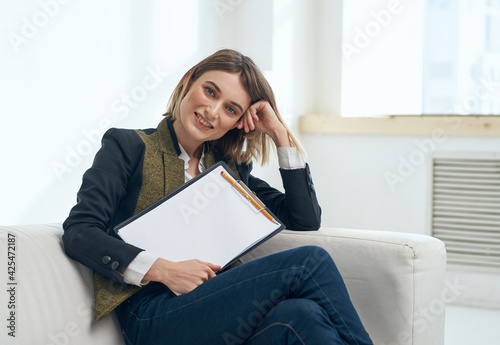 A woman in a jacket and trousers with a white sheet of paper in a folder near the window