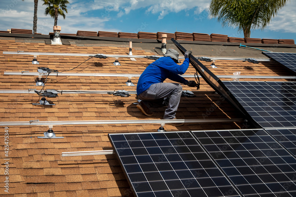 Workers installing solar panels on a tile roofon a sunny day Workers installing solar panels on a tile roofon a sunny day
