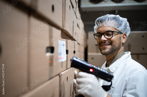 Factory worker scanning food packages with bar code scanner in cold storage.