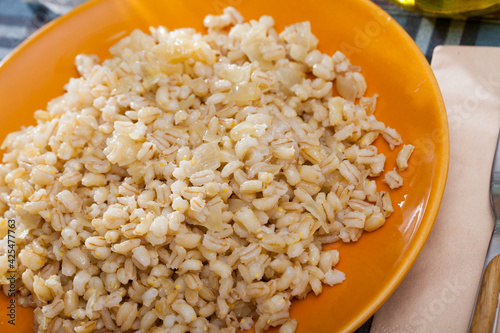 Colorful ceramic plate with cooked pearl barley porridge on checkered textile background photo