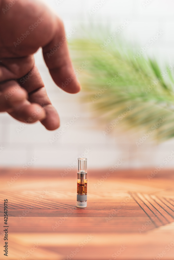 A hand reaches to pick up a cannabis vape cartridge. A hand reaches to pick up a cannabis vape cartridge.