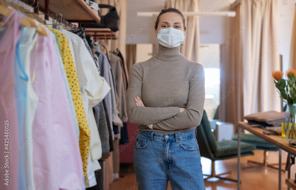 Beautiful happy young woman owner of a clothing store in a protective mask. Small business in a pandemic concept