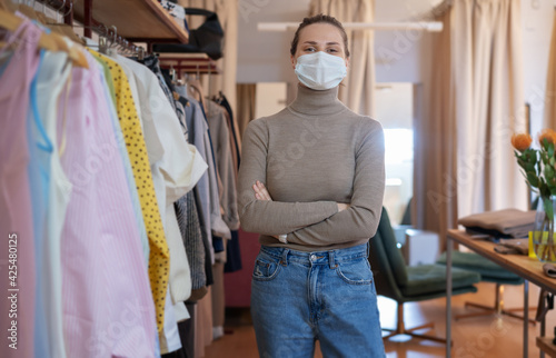 Beautiful happy young woman owner of a clothing store in a protective mask. Small business in a pandemic concept